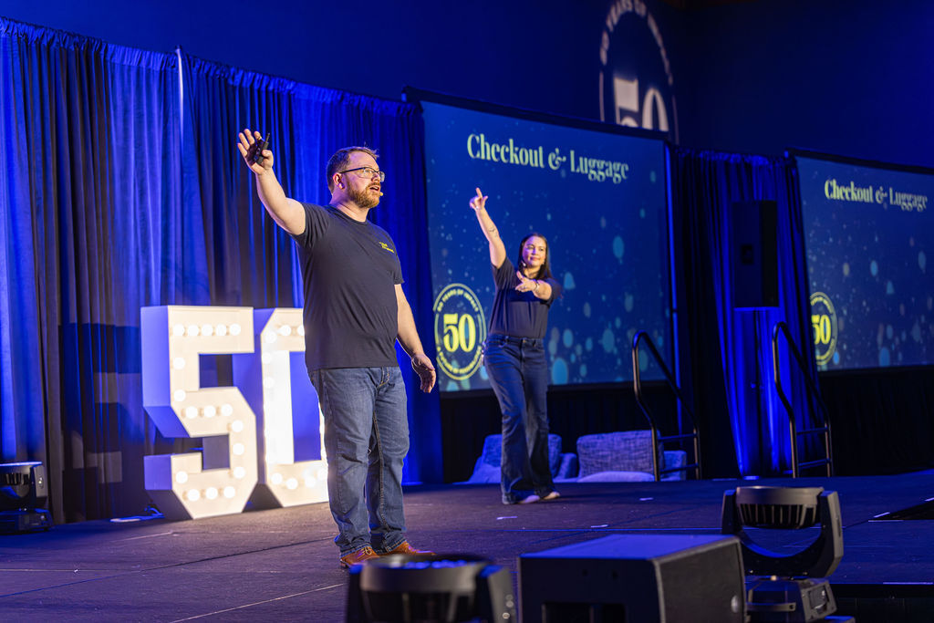 Two presenters on stage at the Bell Partners anniversary conference with illuminated 50 marquee letters
