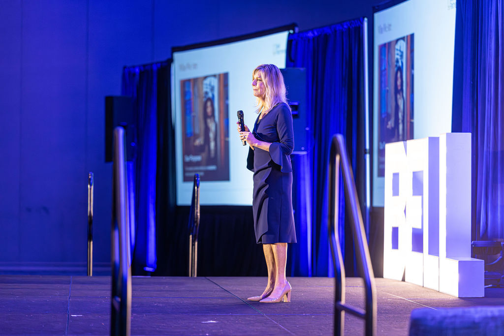 Speaker presenting on stage at a Bell Partners corporate conference with illuminated BELL marquee letters