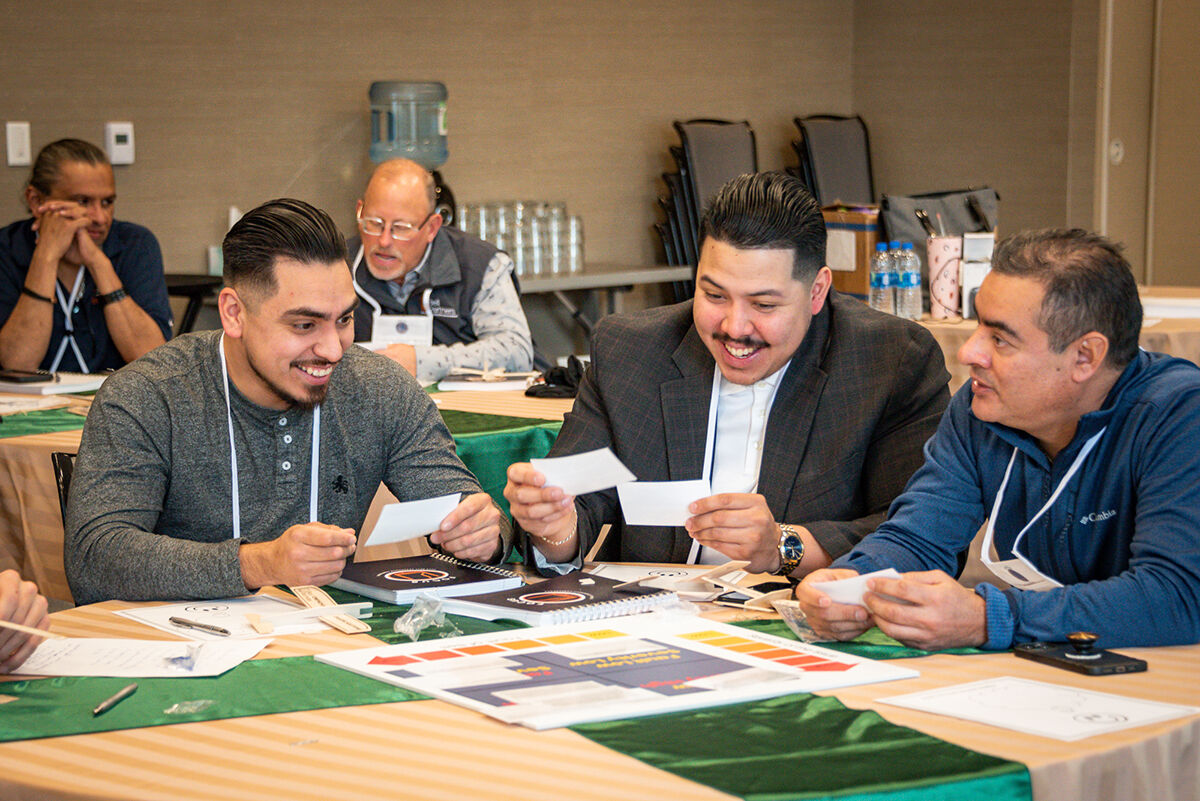 Attendees at a conference workshop table laughing and reviewing documents during a group activity