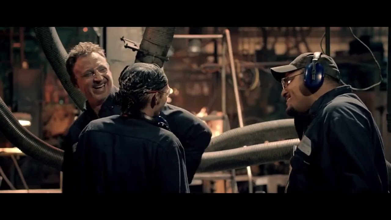 Three men laughing with each other while working in a building with lots of pipes.