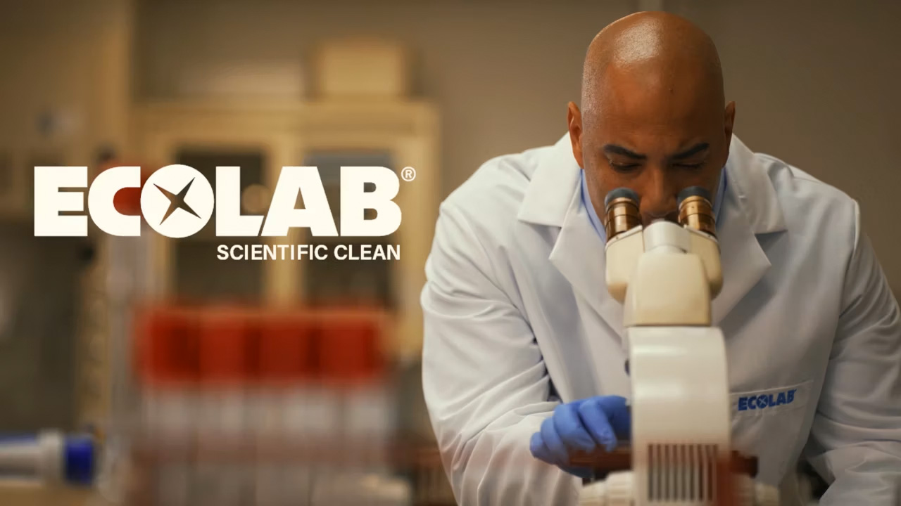 A man looking into a microscope wearing an Ecolab lab coat and the words "Ecolab scientific clean" beside him.