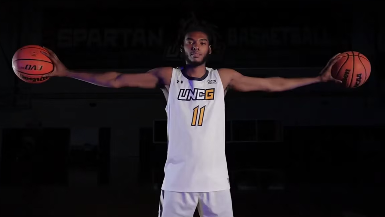 A UNCG basketball player holding two basketballs on either side of him.