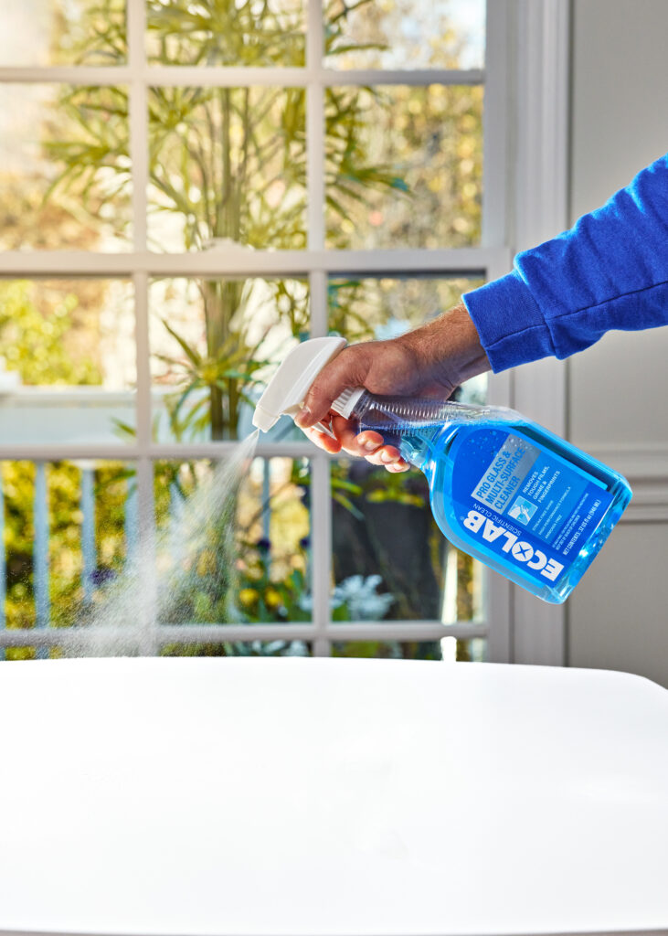 An action shot of someone spraying cleaning chemicals on a kitchen table.