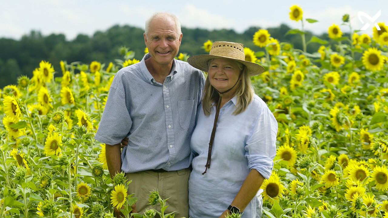 A male and female farmer standing in a field of sunflowers.