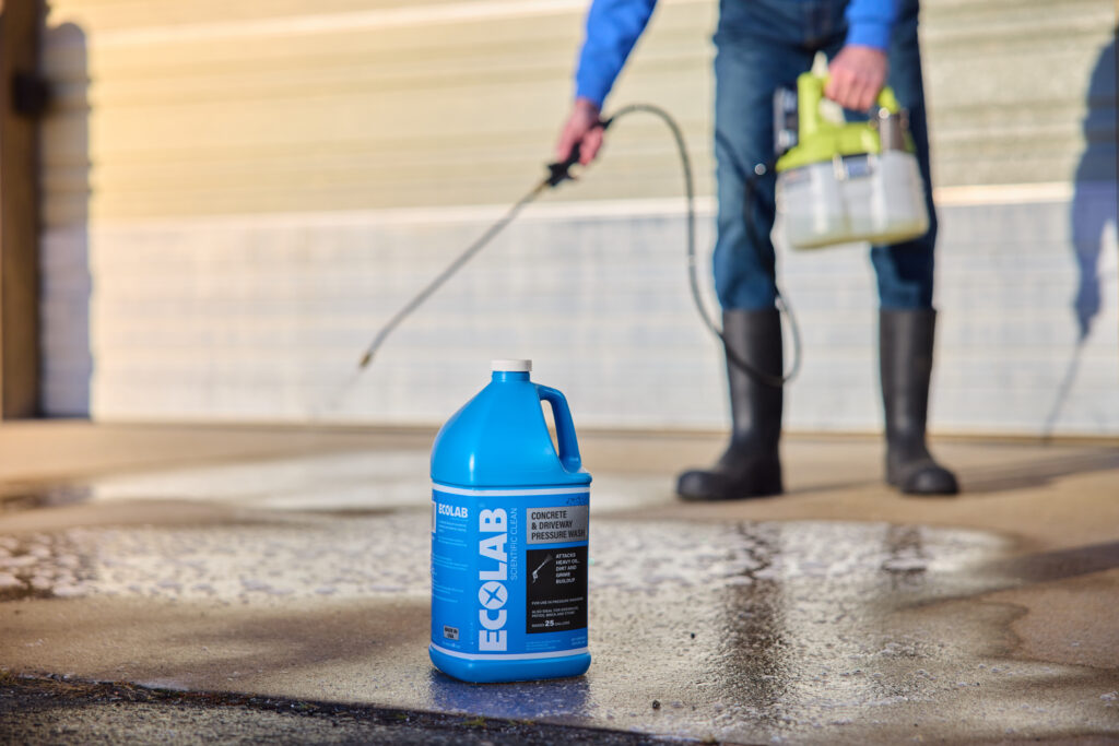 Someone pressure washing concrete with an Ecolab bottle in front.