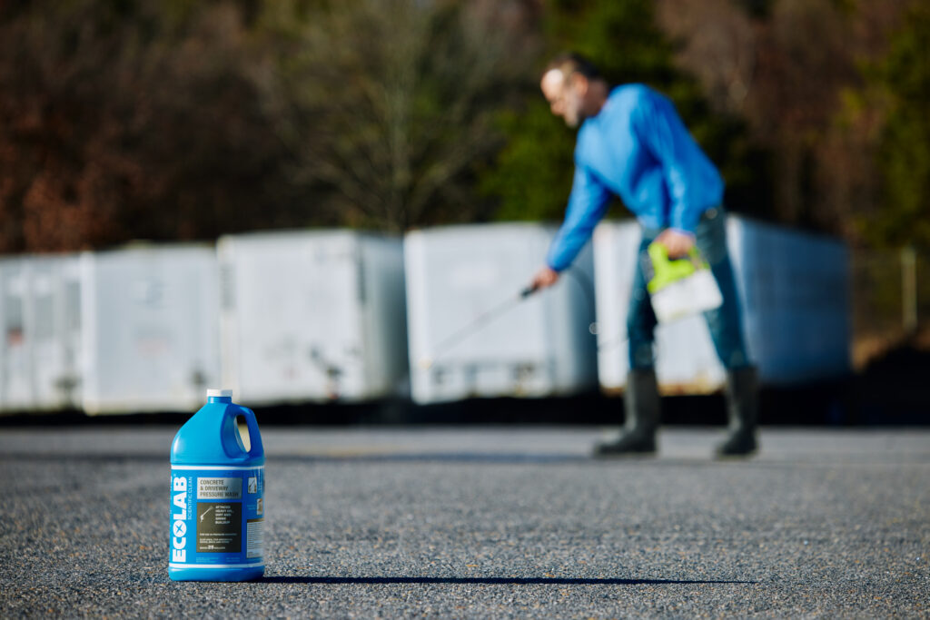 A man power washing concrete with an ecolab bottle in front.