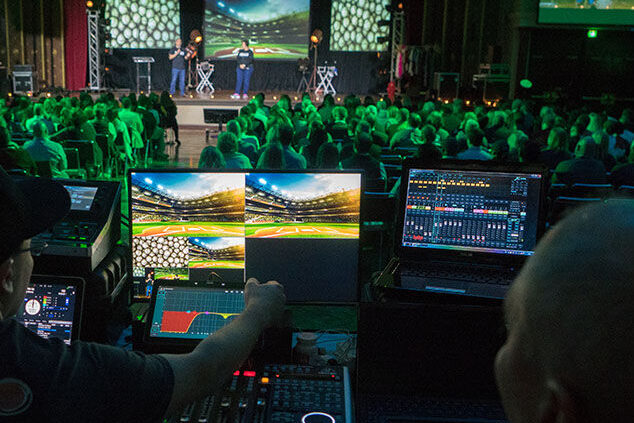 AV operator managing live event monitors at a large corporate conference with full audience