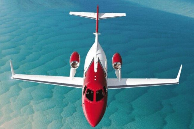 Red and white private jet flying over turquoise coastal waters for commercial photography