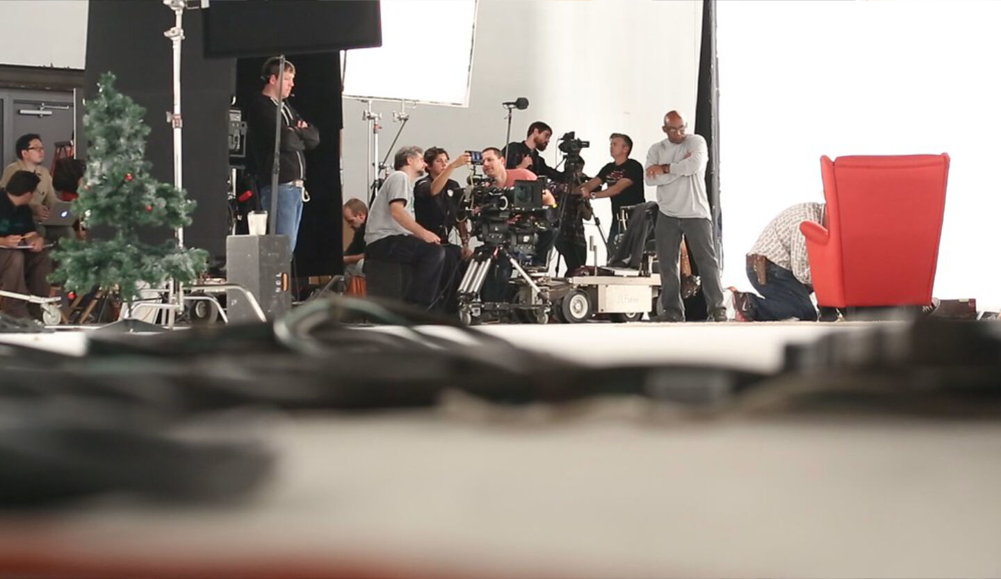 Large film crew shooting holiday TV commercial in studio with camera dolly and Christmas tree