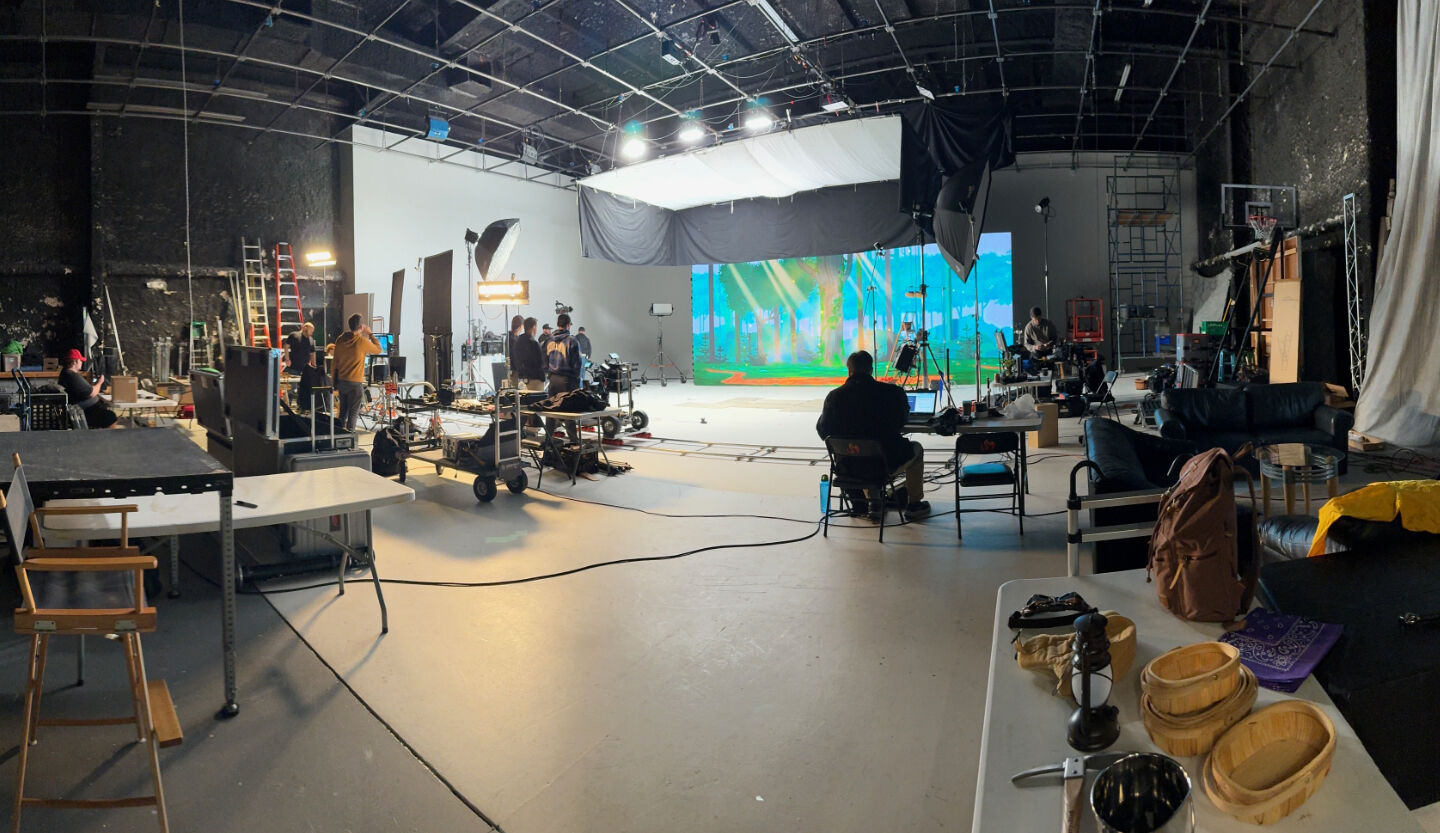 Production crew filming in large studio with LED video wall forest backdrop
