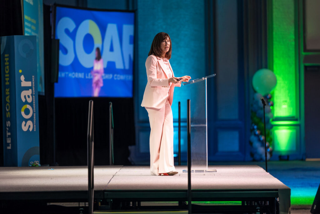 Speaker at the podium at the SOAR Hawthorne Leadership Conference with event branding and stage lighting