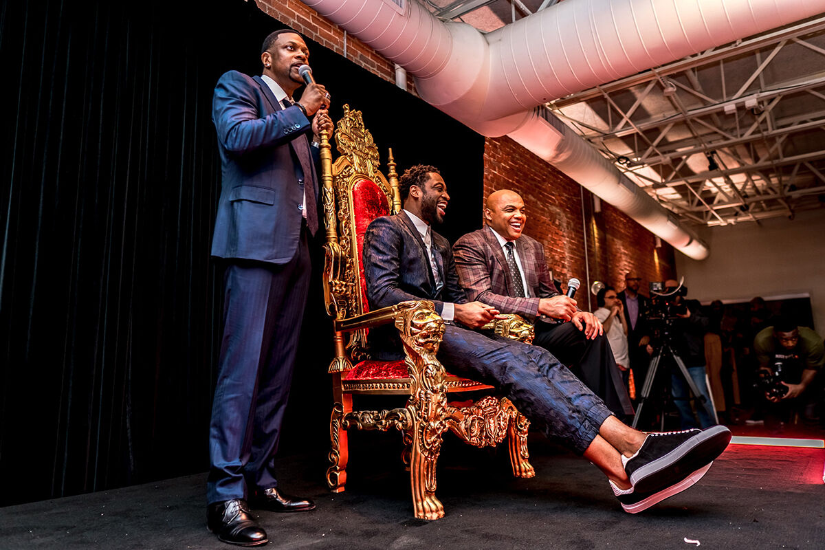 Three men on stage at a celebrity event, one seated in an ornate gold throne chair, captured by K2 Productions