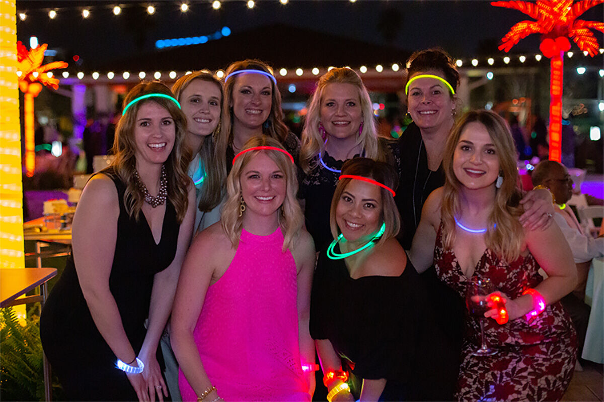 Group of women wearing glow accessories smiling at an outdoor evening corporate party event