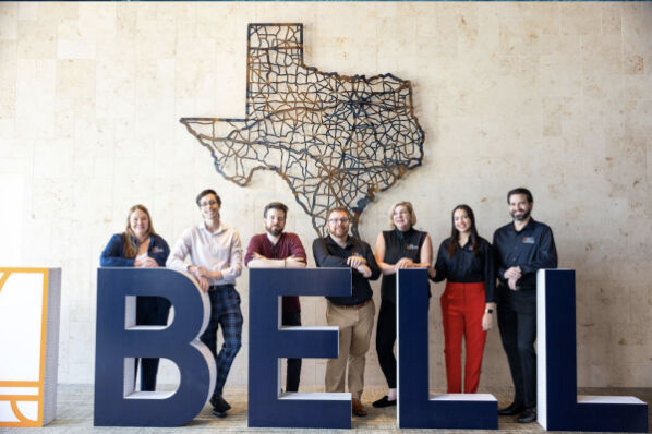 Bell Partners team posing with large BELL block letters in front of a Texas state wall art display