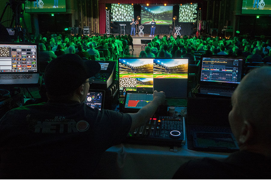 AV technician managing video content on a multi-screen production control station at a corporate event