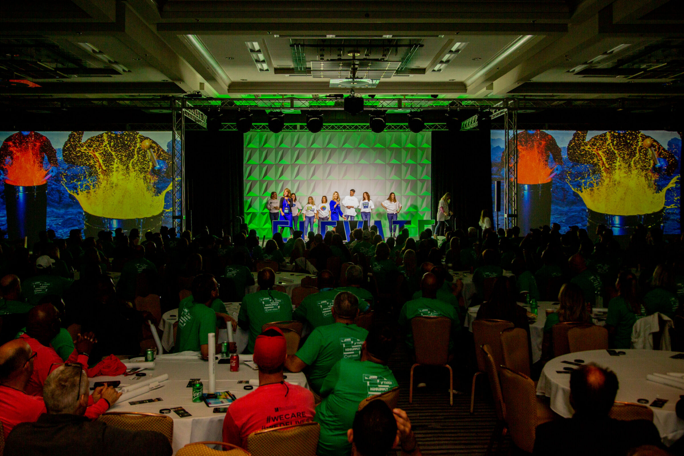 Group of presenters on stage at a corporate conference with green lighting and large audience, K2 Productions event staging